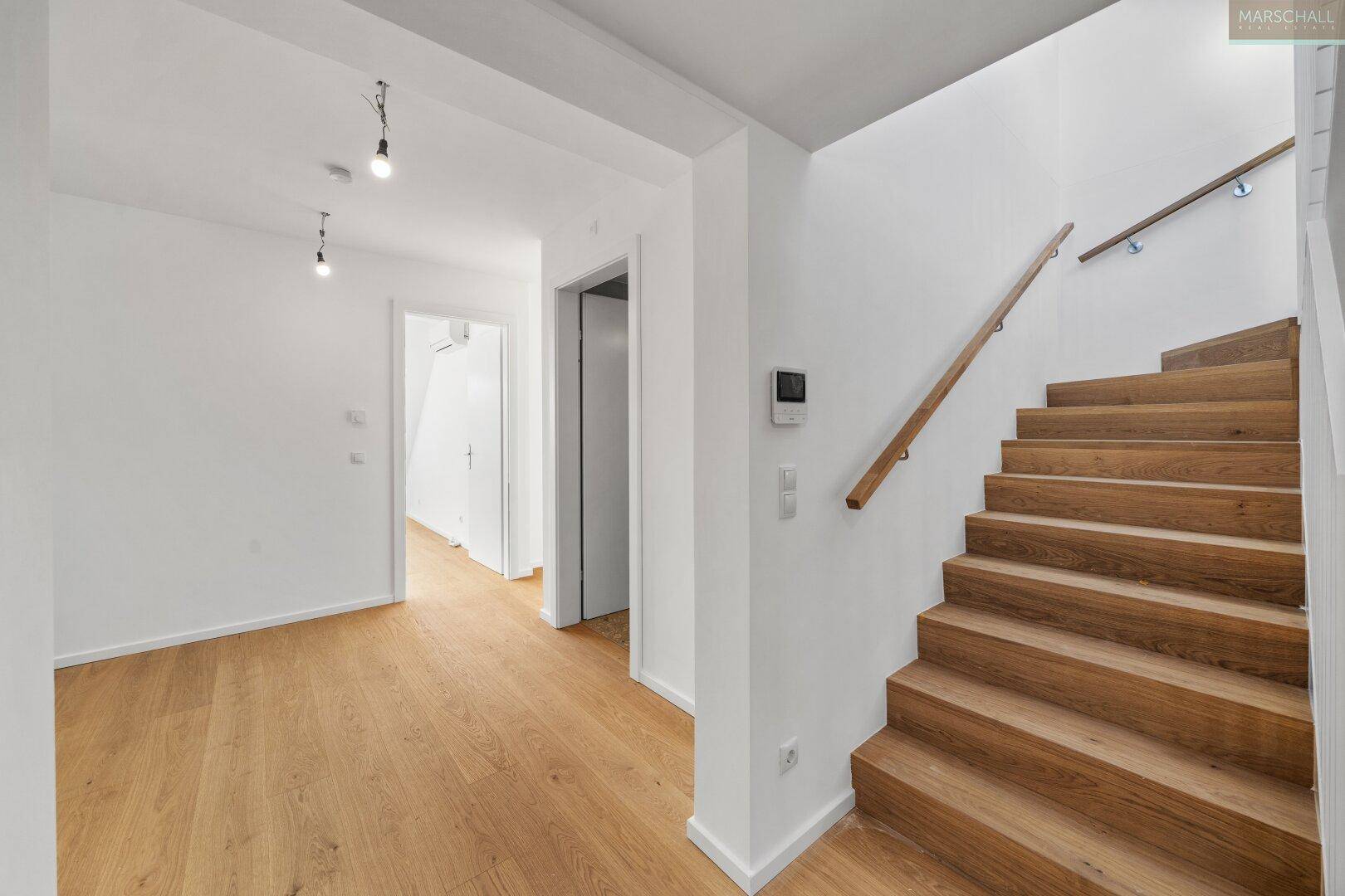 Heller Flur mit Holztreppe und Parkettboden, der zu weiteren Räumen führt.