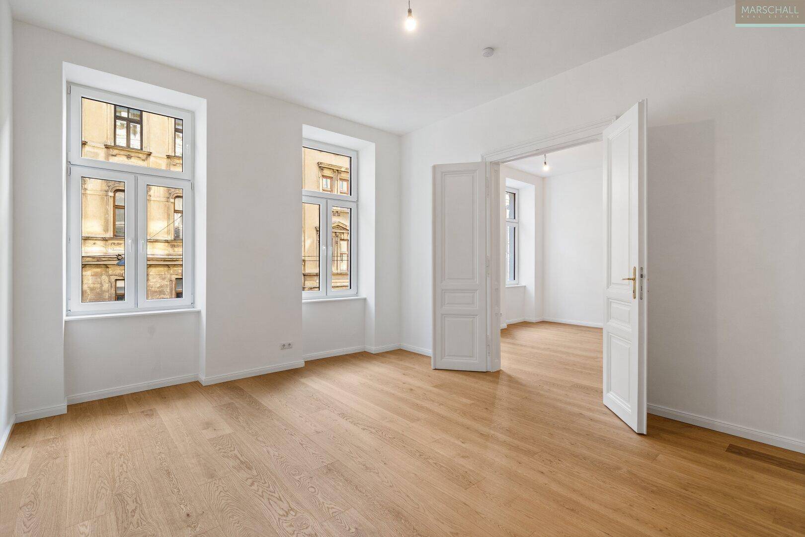 Geräumiger, heller Wohnraum mit neuem Parkettboden und großen Fenstern, die den Blick auf die Umgebung freigeben.