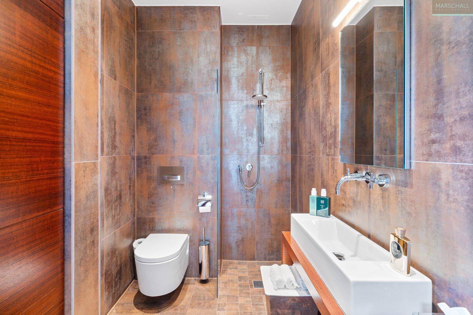 Modernes Badezimmer mit begehbarer Dusche, Wand-WC und eleganten Fliesen in Rostoptik.