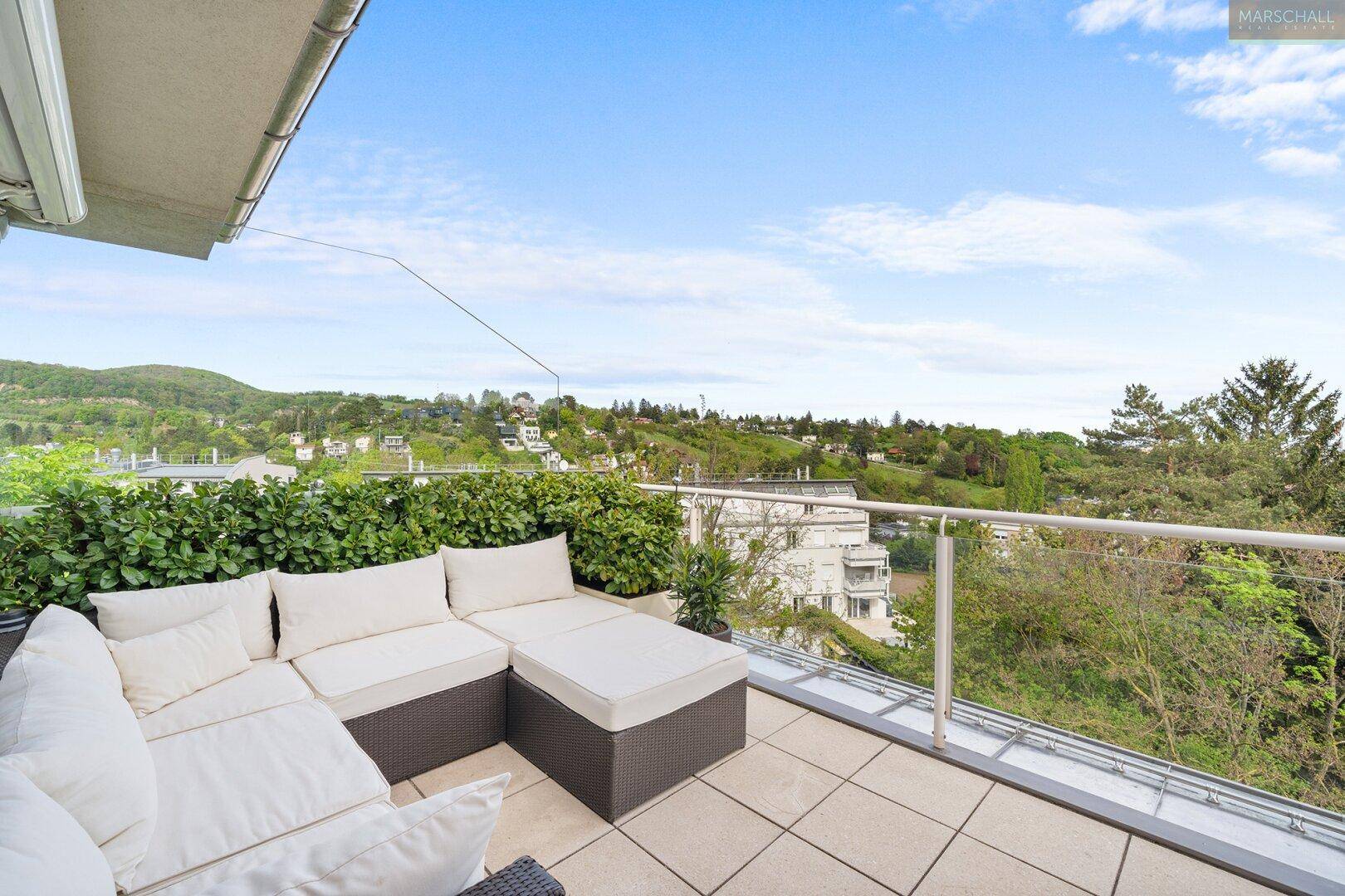 Geräumige Terrasse mit Lounge-Möbeln, Hecke und weitem Blick über die grüne Landschaft.