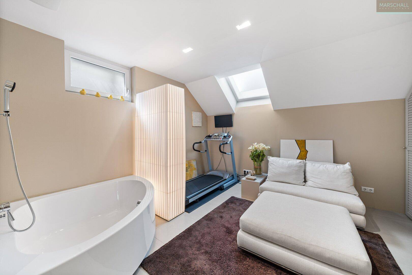 Wellnessbereich mit Badewanne, Laufband und Sitzgelegenheit unter einem Dachfenster.