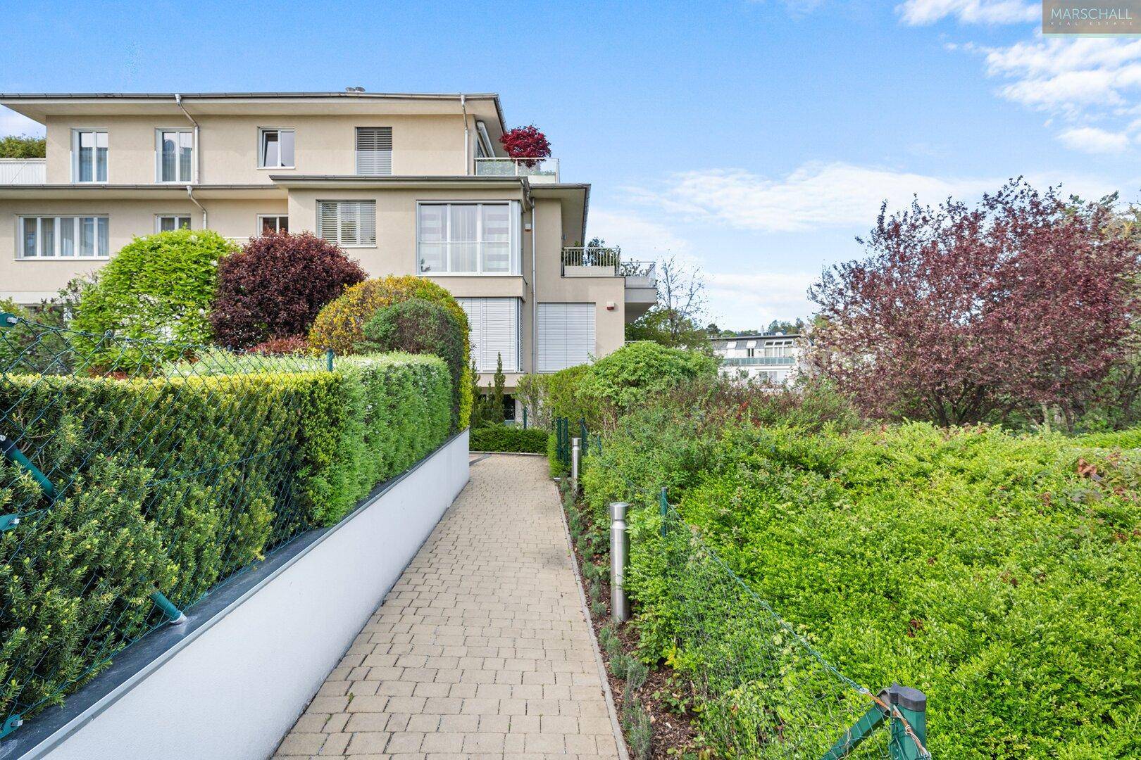 Gepflegter Gartenweg führt zu einem modernen Wohngebäude, umgeben von viel Grün.