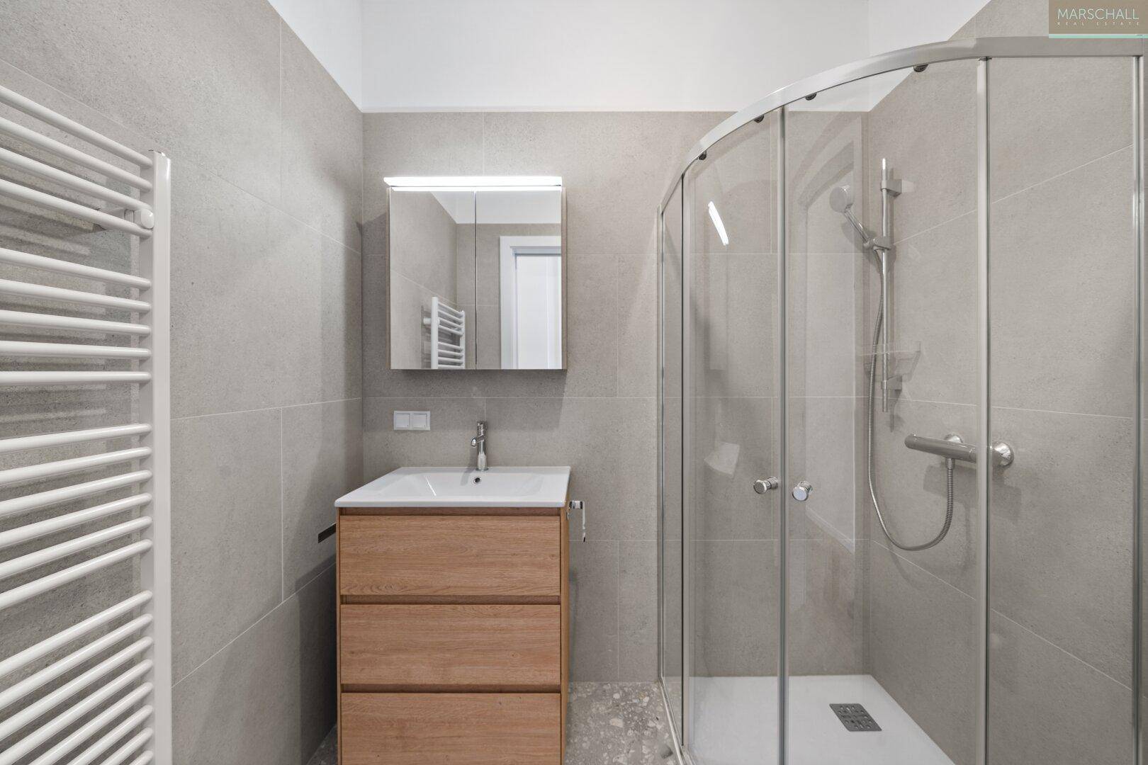 Modernes Badezimmer mit grauen Fliesen, Duschkabine und beheiztem Handtuchhalter.