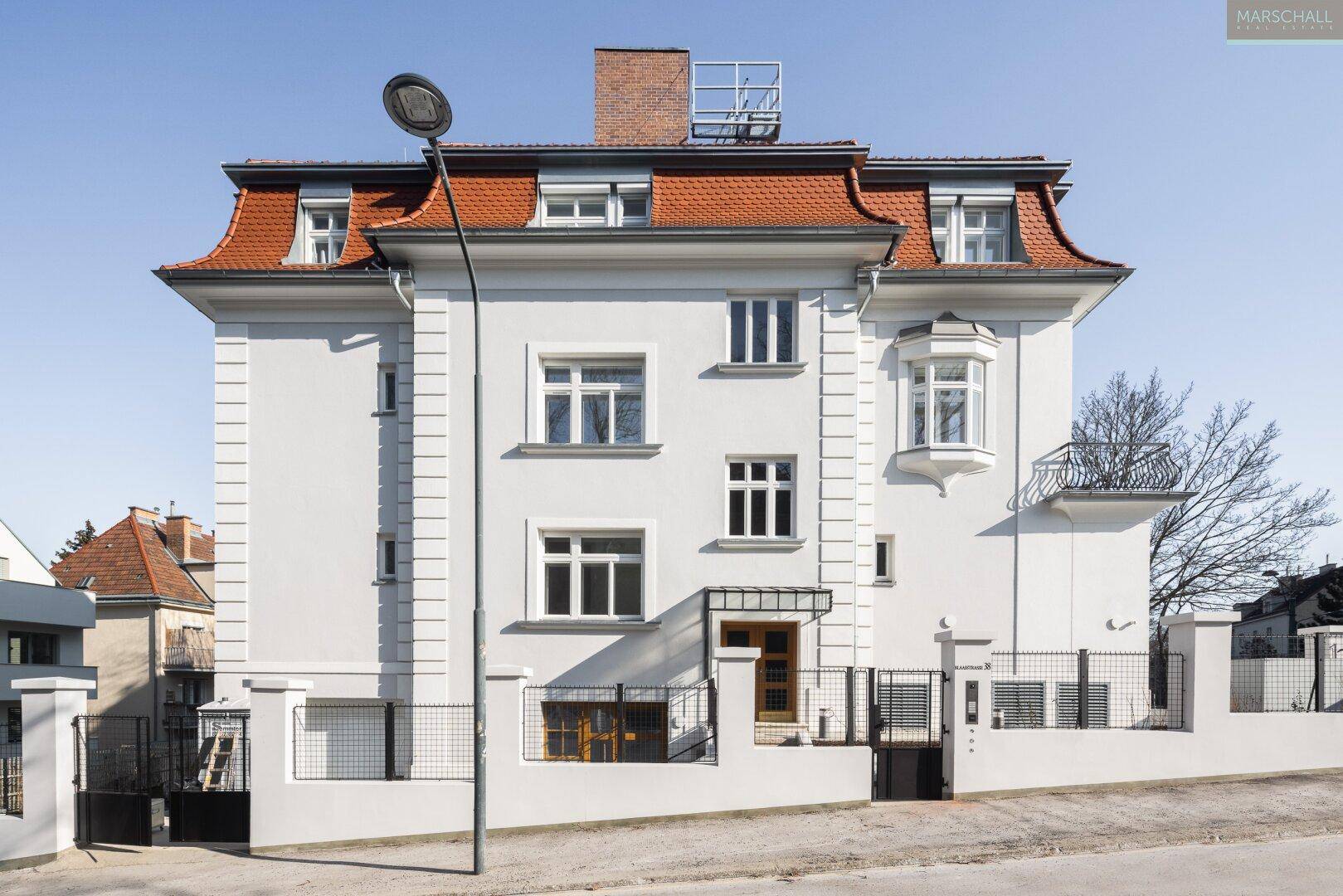 Elegante Villa mit weißer Fassade, rotem Mansarddach und markantem Erker.