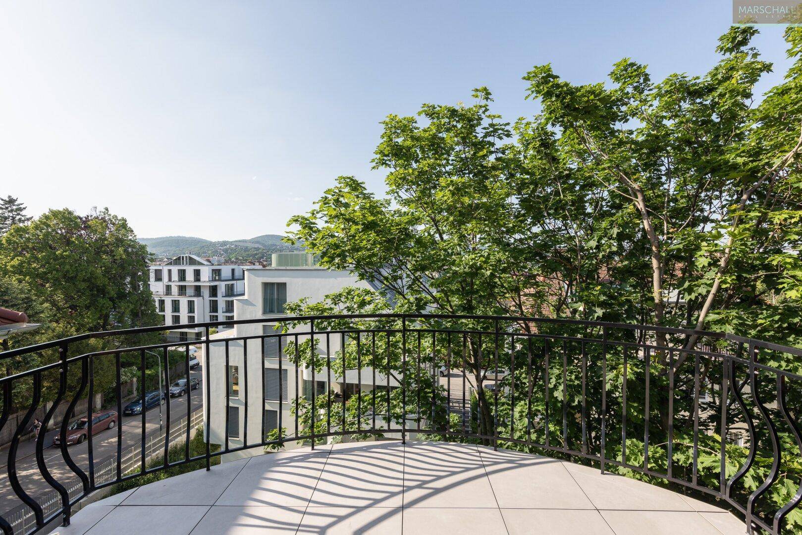Runder Balkon mit schmiedeeisernem Geländer und Blick auf die umliegenden Gebäude und Bäume.