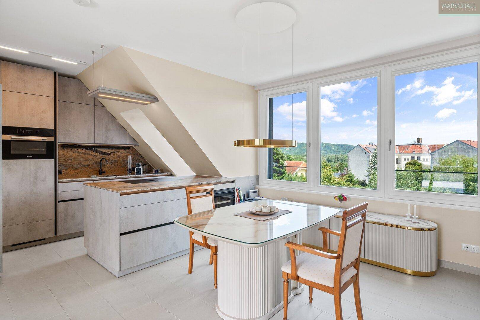 Moderne Küche mit Dachschrägen, Essbereich und weitem Blick ins Grüne durch große Fenster.