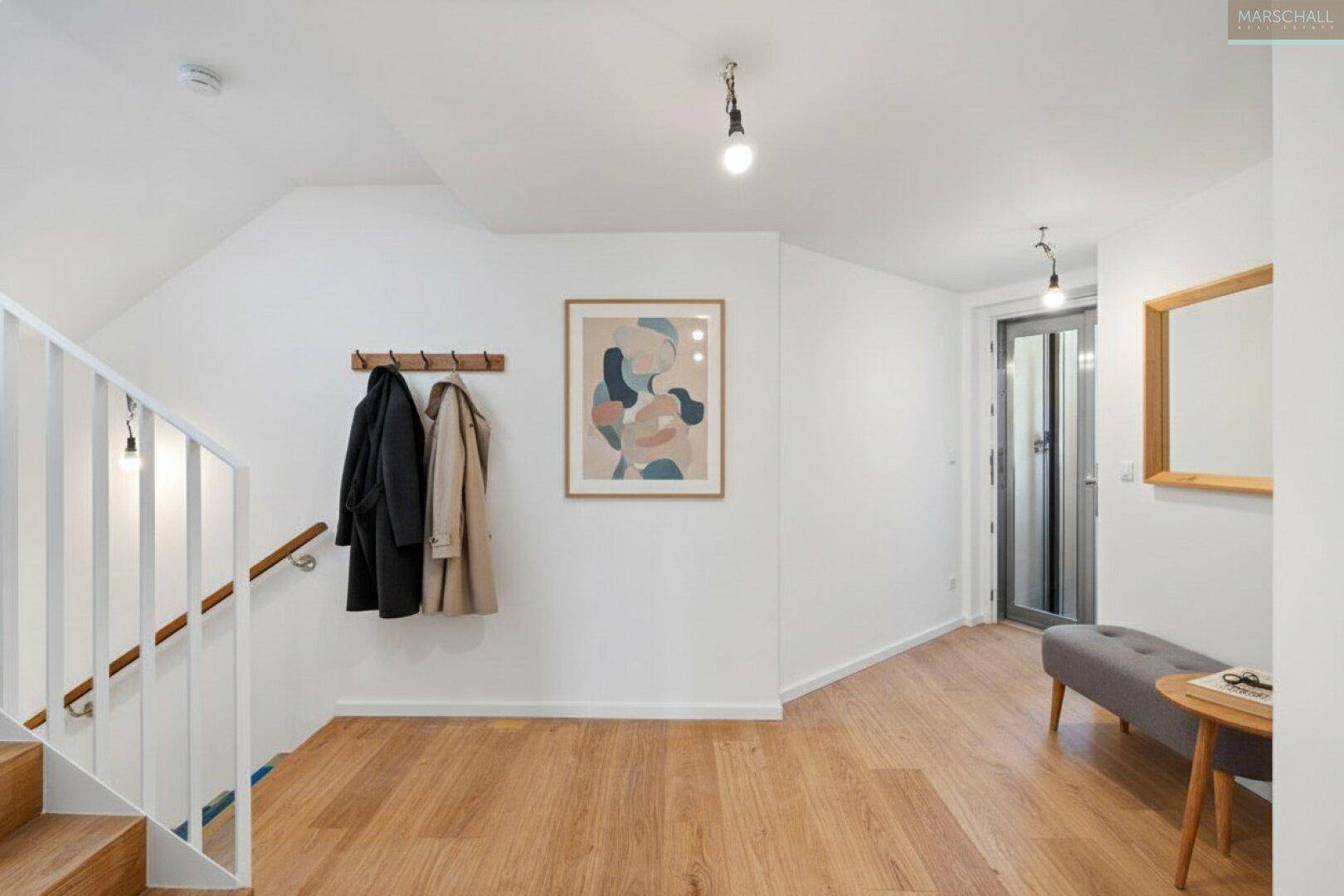 Heller Eingangsbereich mit Holztreppe, Garderobe und modernem Dekor, einladend gestaltet.