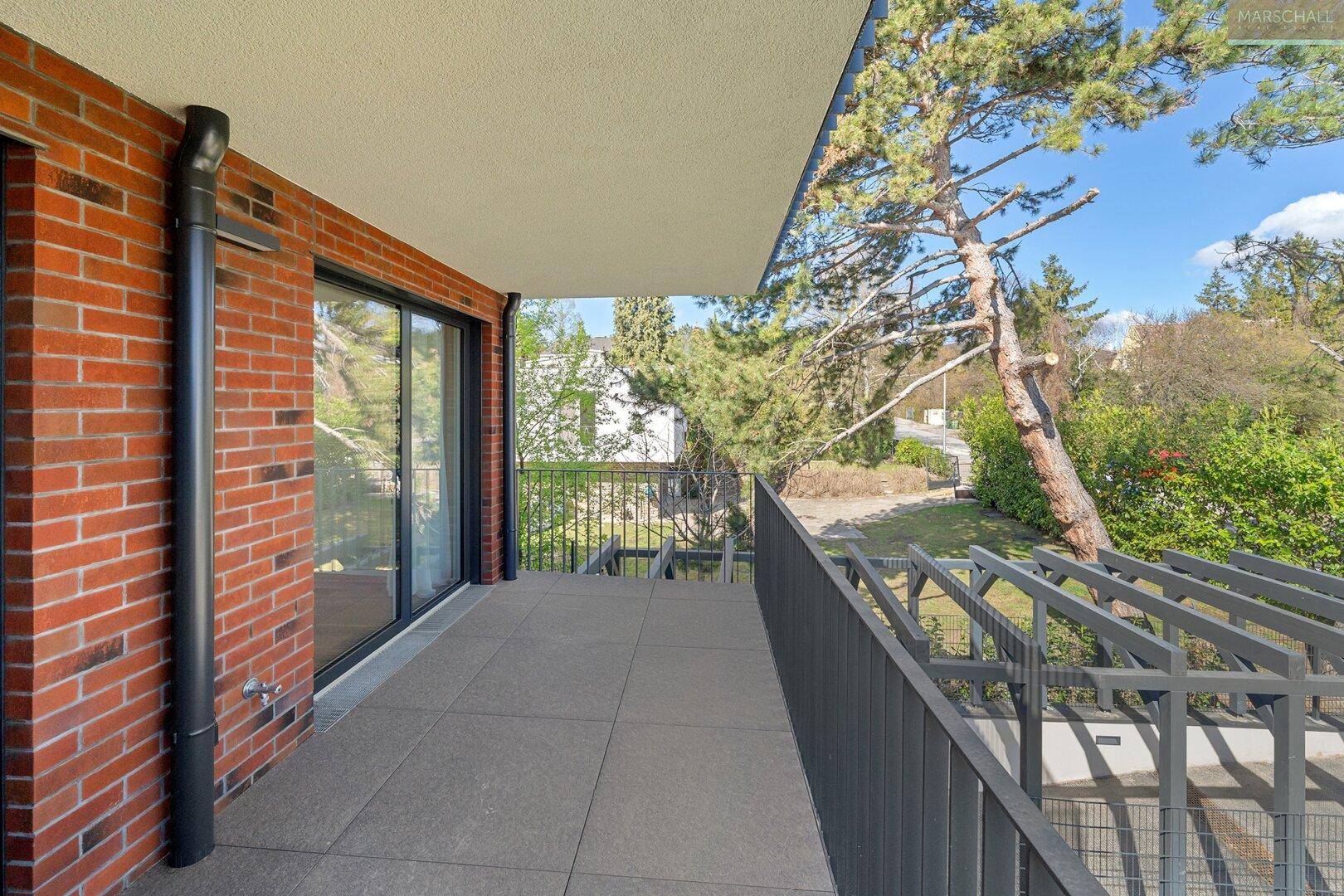 Geräumiger Balkon mit Fliesenboden, Ziegelwand und Blick auf Bäume und Umgebung.