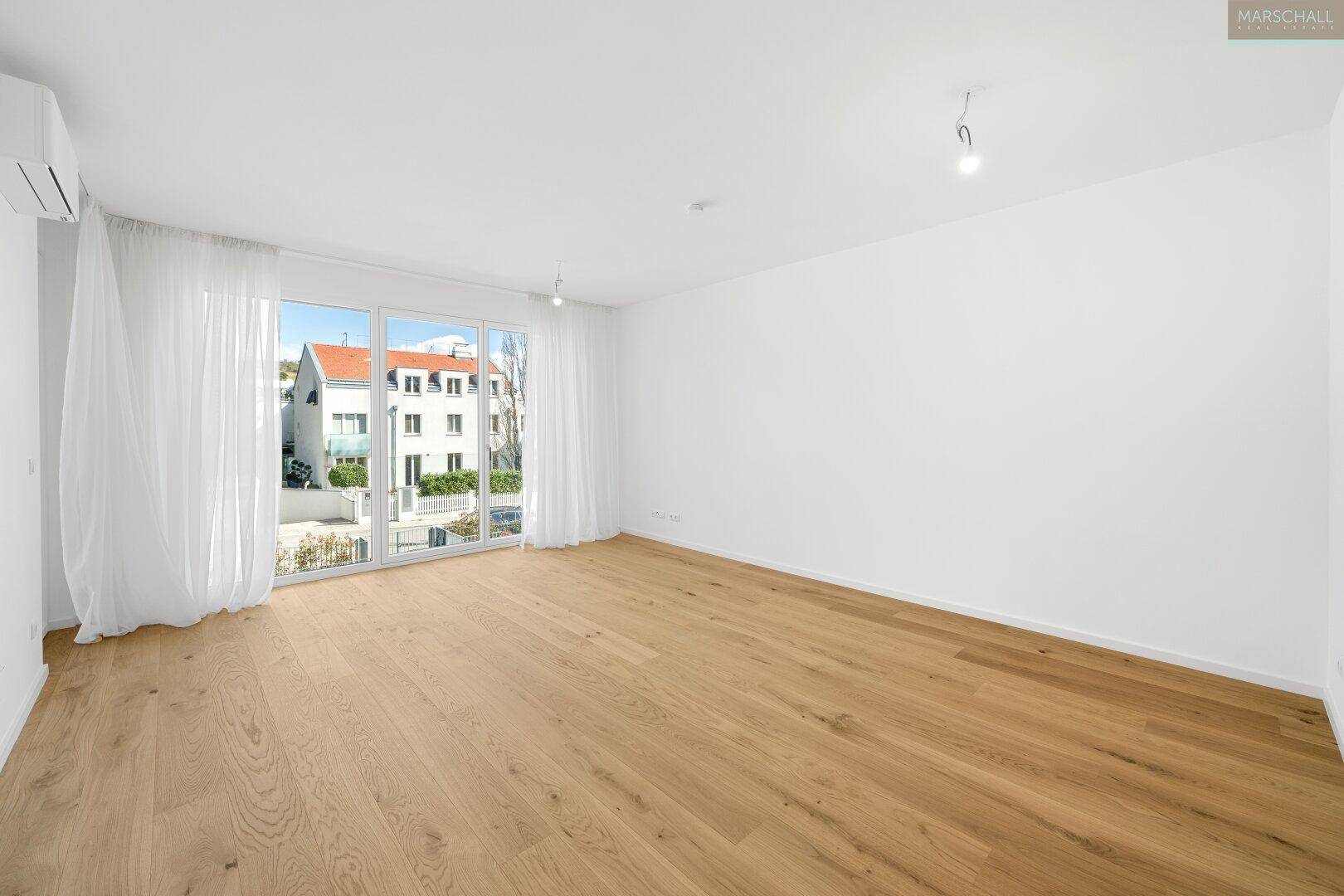 Geräumiges Wohnzimmer mit hellem Parkettboden, großen Fenstern und Blick auf die Nachbarschaft.