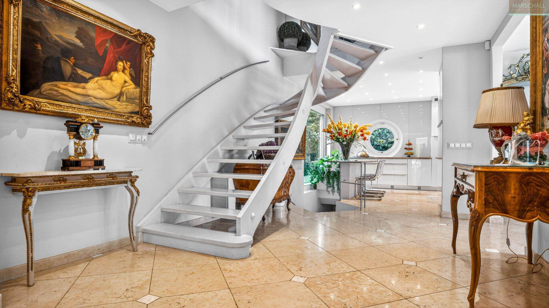 Eleganter Eingangsbereich mit geschwungener Treppe und Blick auf die moderne Küche im Hintergrund.