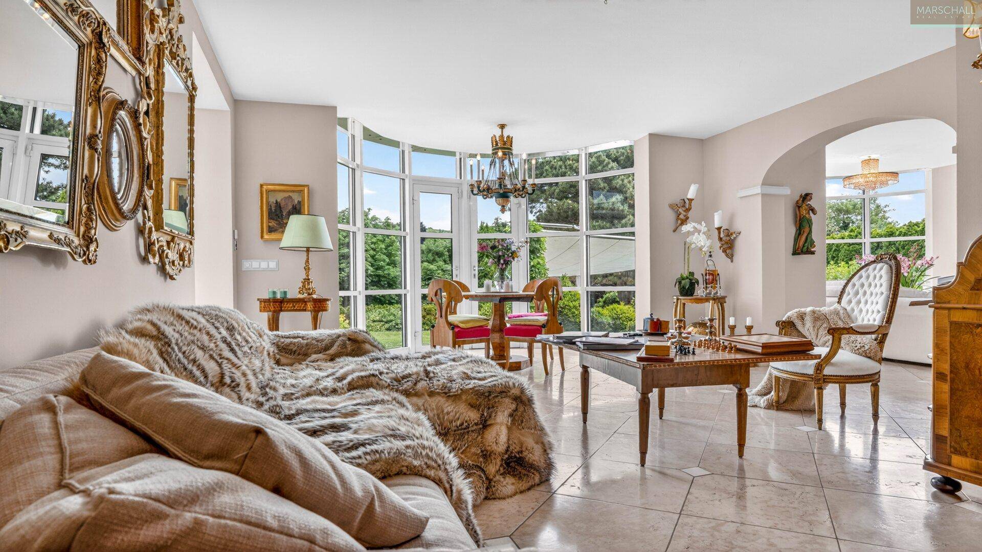 Gemütliches Wohnzimmer mit luxuriösem Sofa, großem Spiegel und Blick auf die grüne Umgebung.