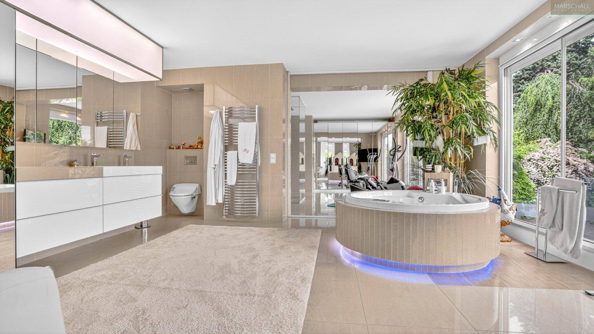 Luxuriöses Badezimmer mit großem Whirlpool, Doppelwaschbecken und Blick in den Garten.
