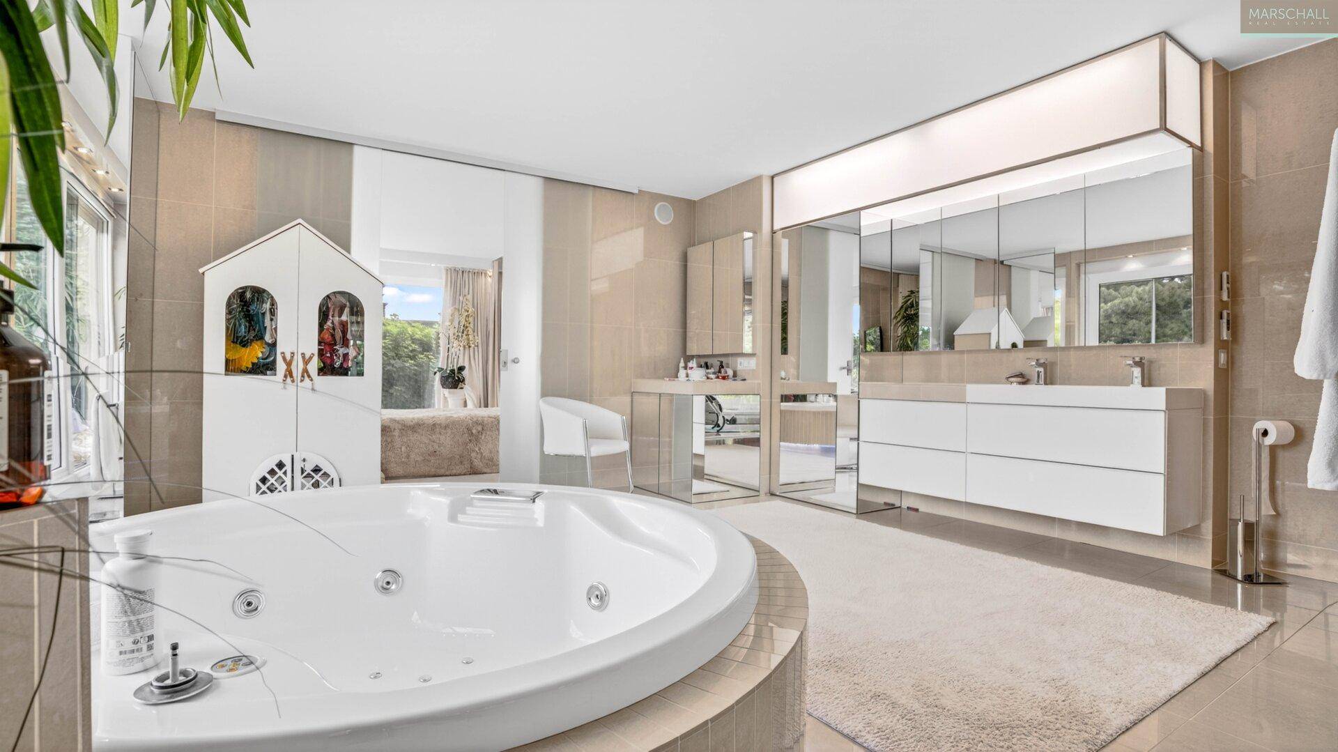 Geräumiges Luxusbad mit rundem Whirlpool, Schminktisch und großem Spiegelschrank.