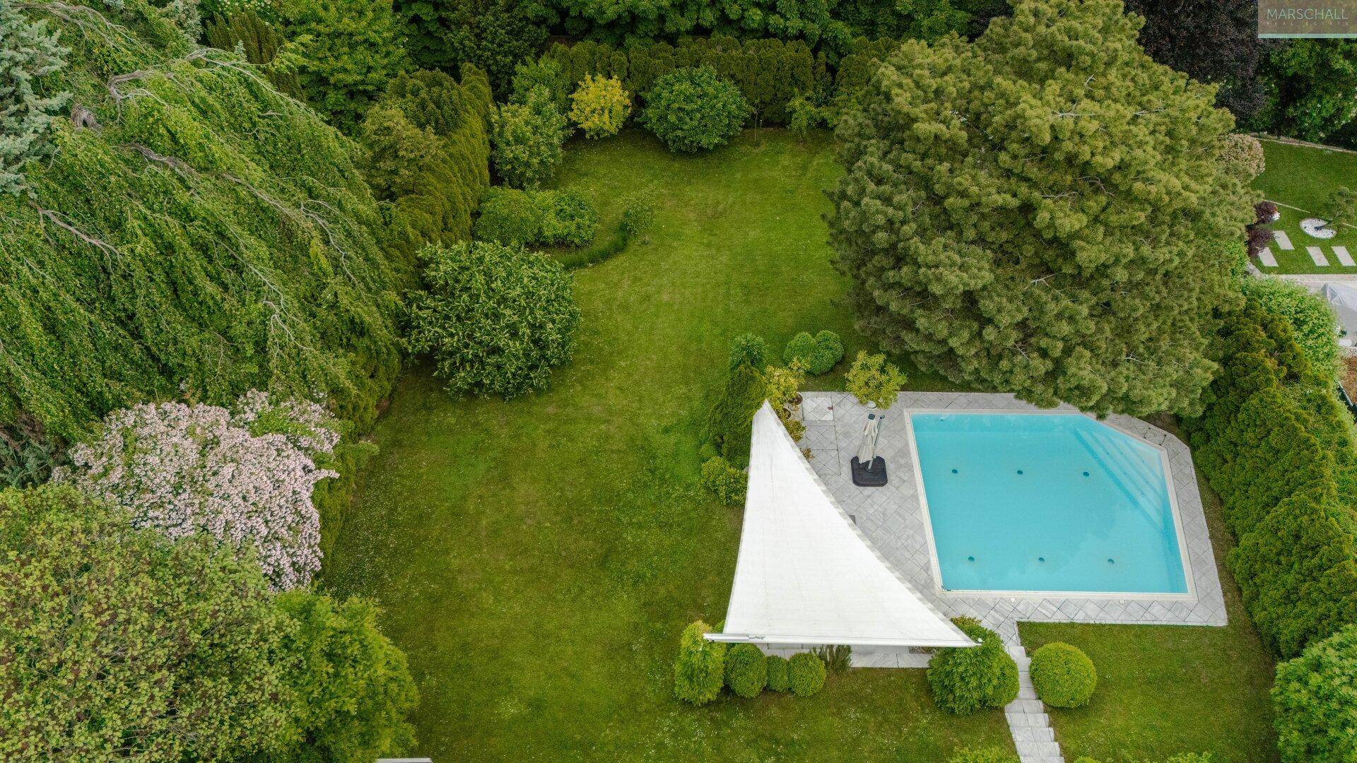 Weitläufiger Garten mit großem Rasen, Swimmingpool und üppiger, gepflegter Bepflanzung.