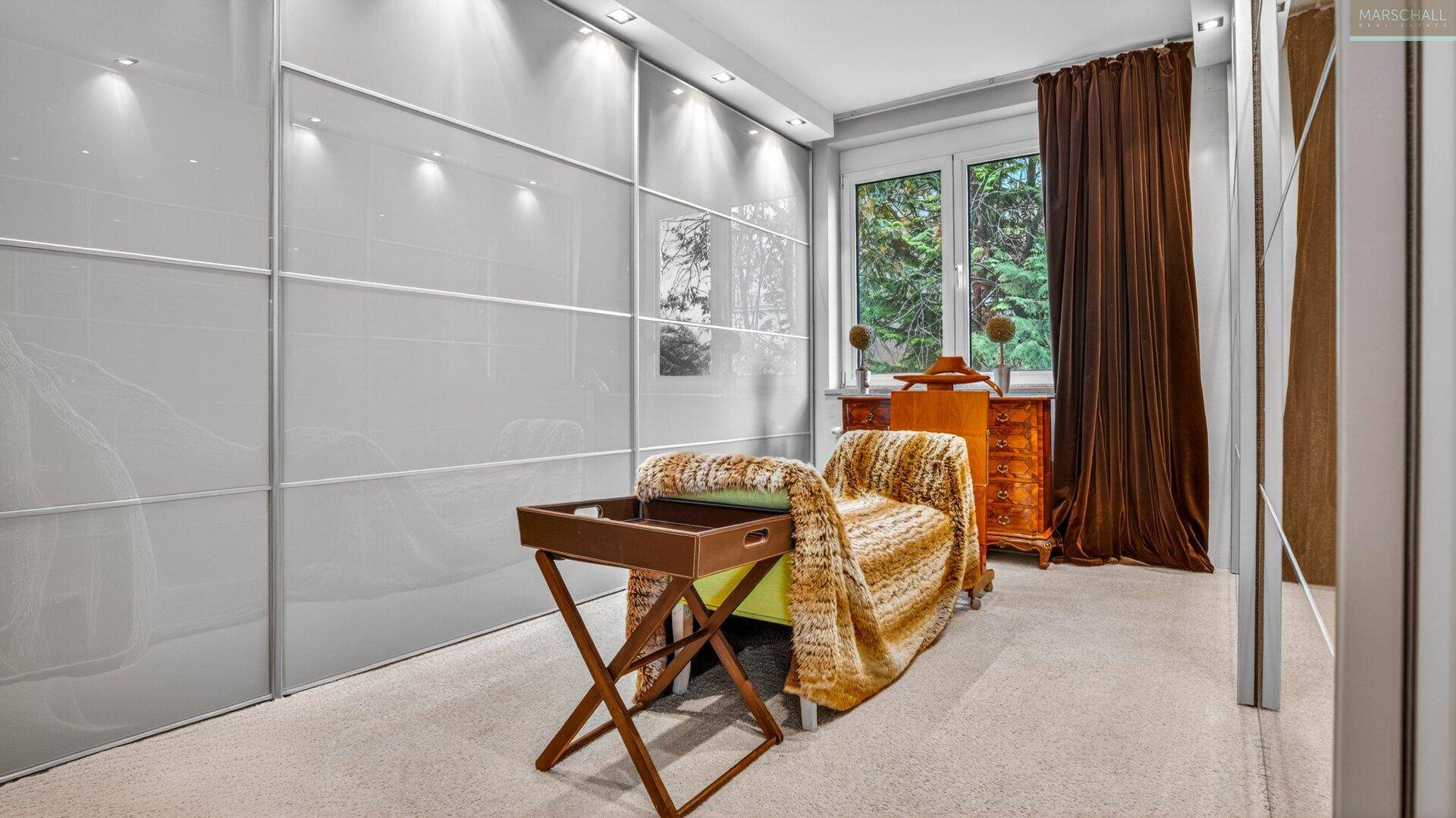Gemütliches Schlafzimmer mit hellen Schiebetürenschränken, einer Chaiselongue und Blick ins Grüne.