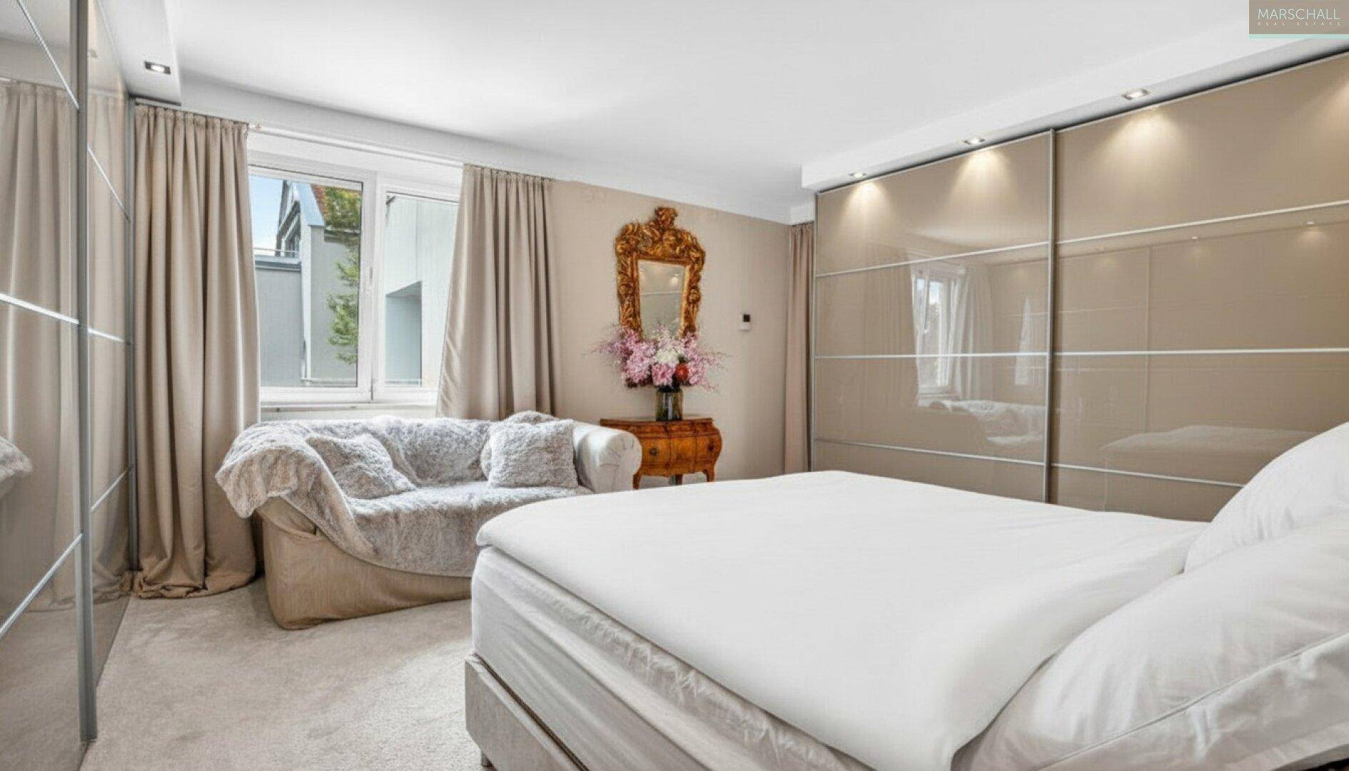 Elegantes Schlafzimmer mit bequemen Bett, Sofa und glänzenden Einbauschränken.