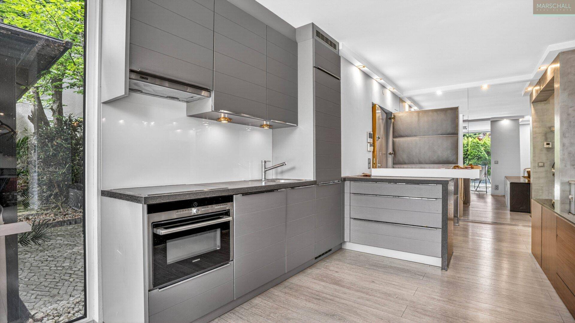 Moderne Küche mit grauen Schränken, integriertem Backofen und Blick auf einen kleinen Außenbereich.