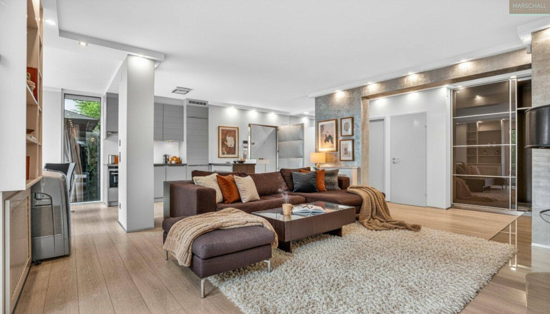 Geräumiges Wohnzimmer mit bequemer Couch, hellem Teppich und offener Verbindung zur Küche.