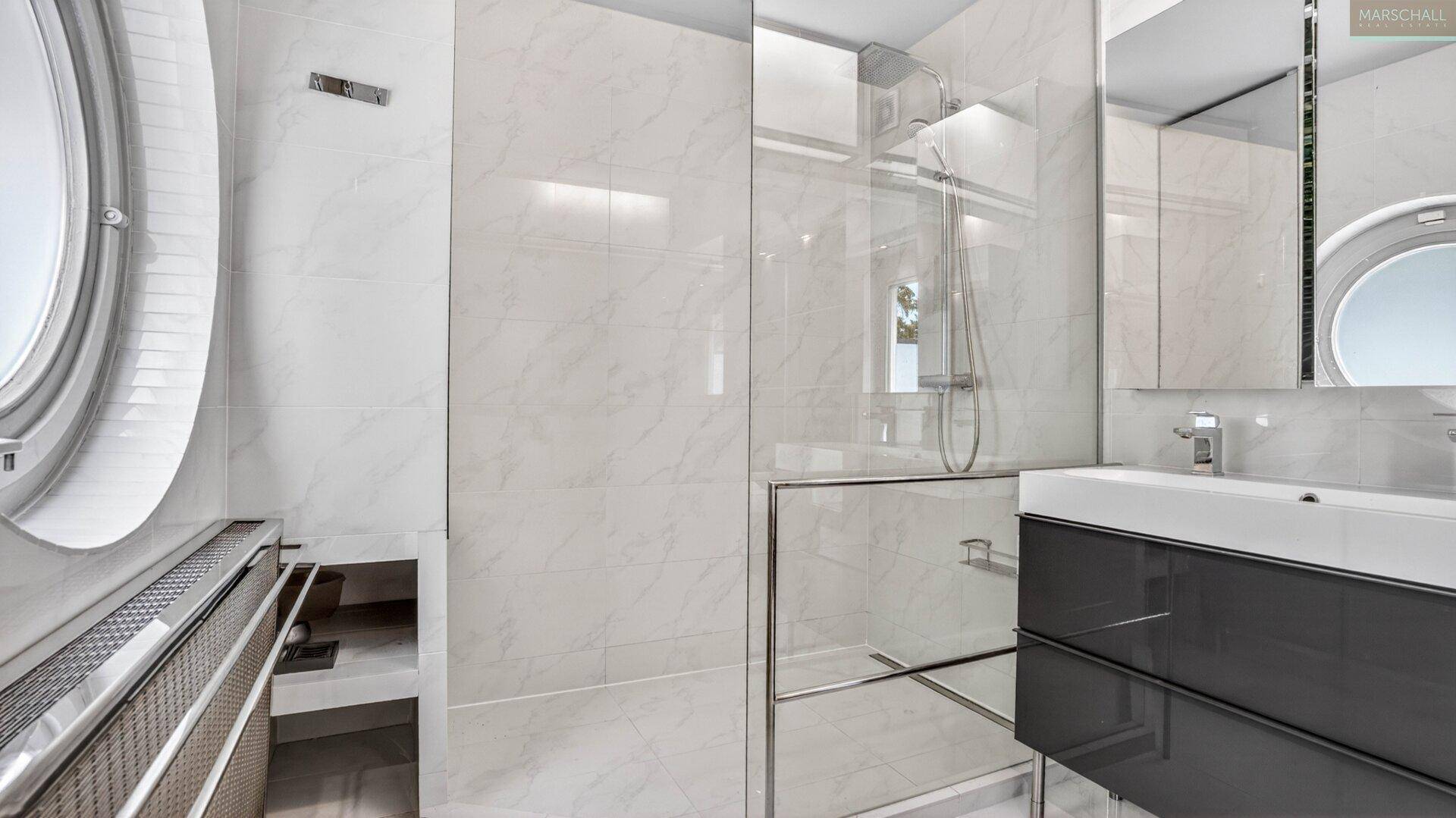 Elegantes Badezimmer mit modernen Marmorfliesen, begehbarer Dusche und stilvollem runden Fenster.