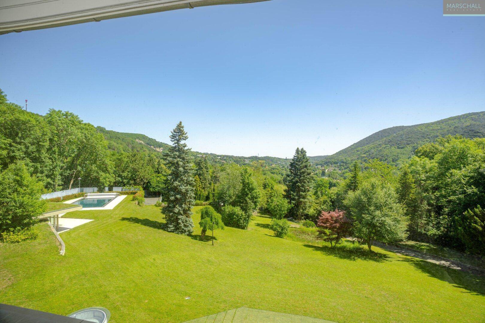 Weitläufiger Gartenbereich mit großem Pool und Panoramablick auf die umliegende grüne Landschaft und Berge.