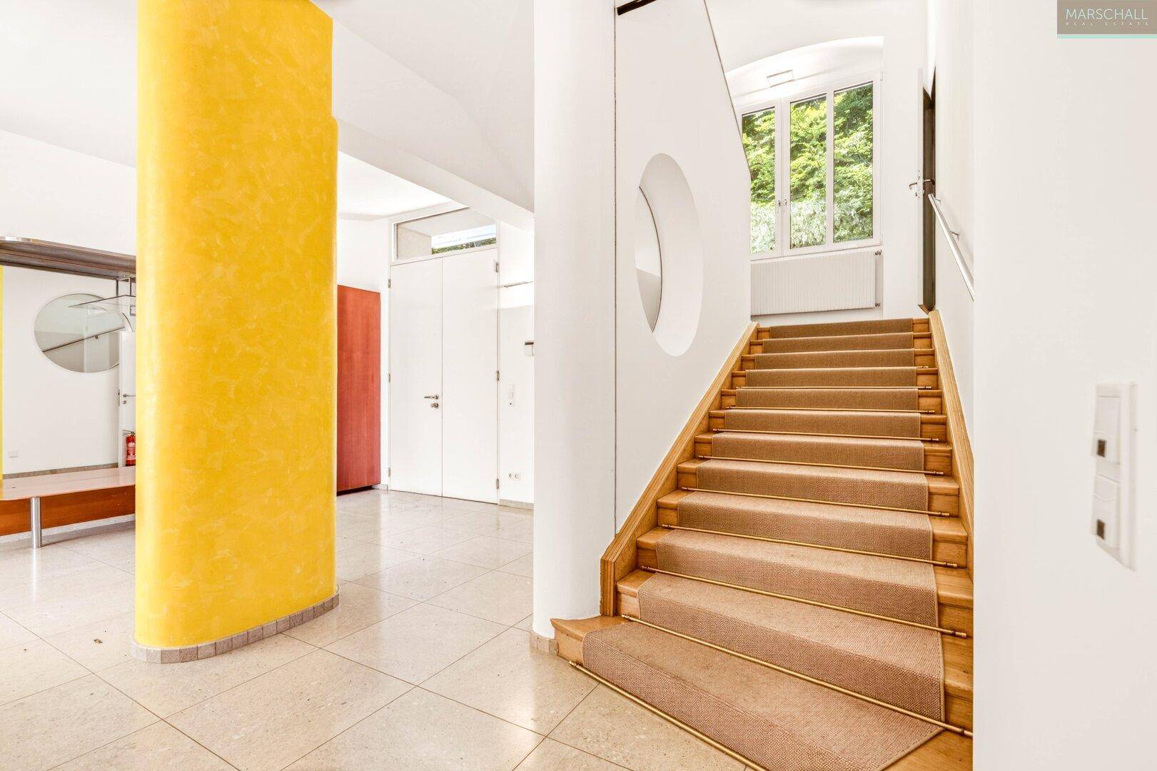 Heller Flur mit Treppe, Teppichboden und dekorativer gelber Säule.