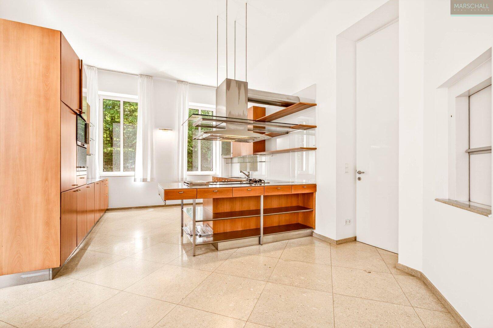 Moderne Küche mit Holzschränken, Kochinsel und Blick ins Grüne.