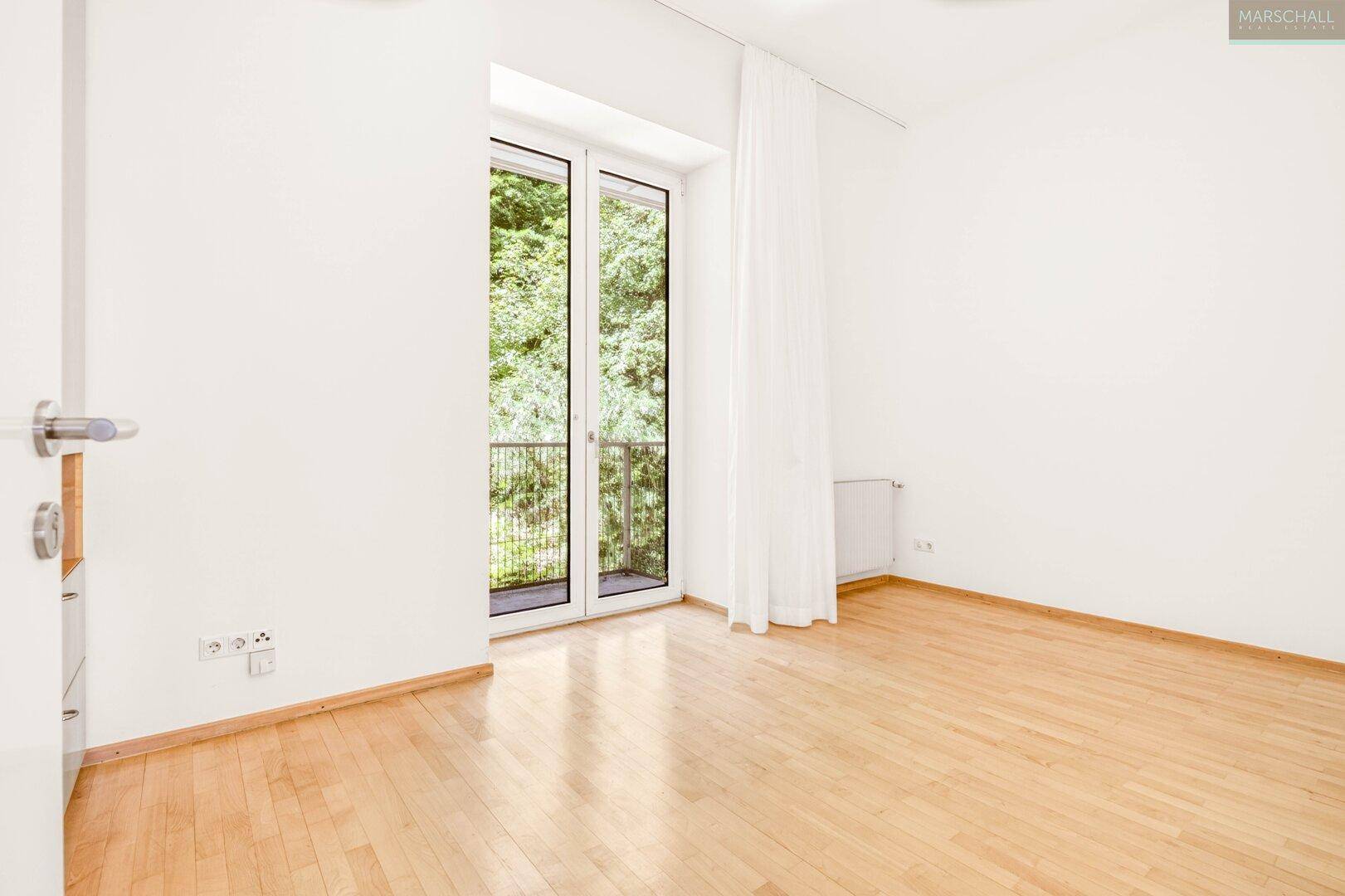 Helles, leeres Schlafzimmer mit Holzboden und Zugang zu einem französischen Balkon.