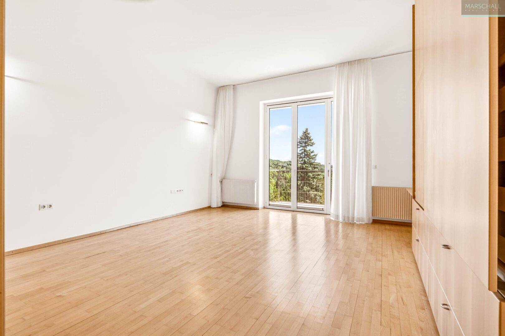 Leeres Schlafzimmer mit Holzboden und Zugang zu einem französischen Balkon.