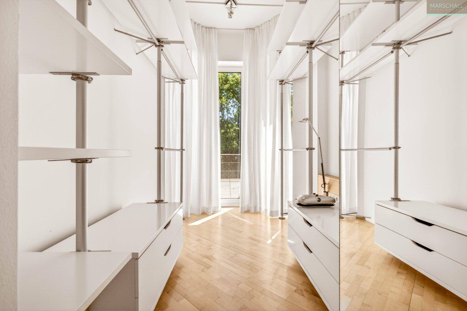 Heller begehbarer Kleiderschrank mit Regalen, Schubladen und Zugang zu einem französischen Balkon.