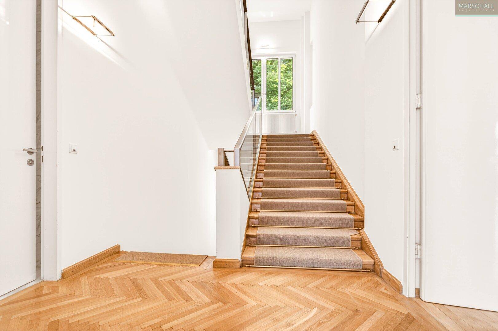 Eleganter Flur mit Holztreppe, Teppichläufer und Fischgrätparkettboden.