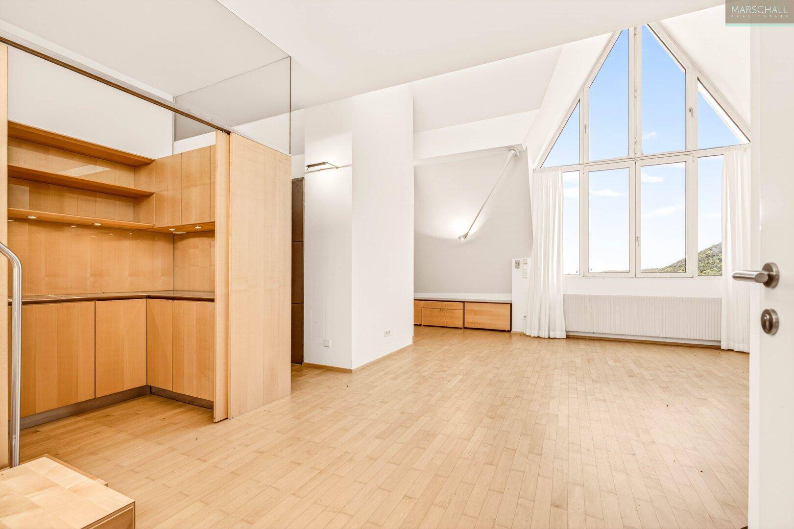 Heller Wohnbereich mit integrierter Küchenzeile, hohen Fenstern und schrägen Decken.