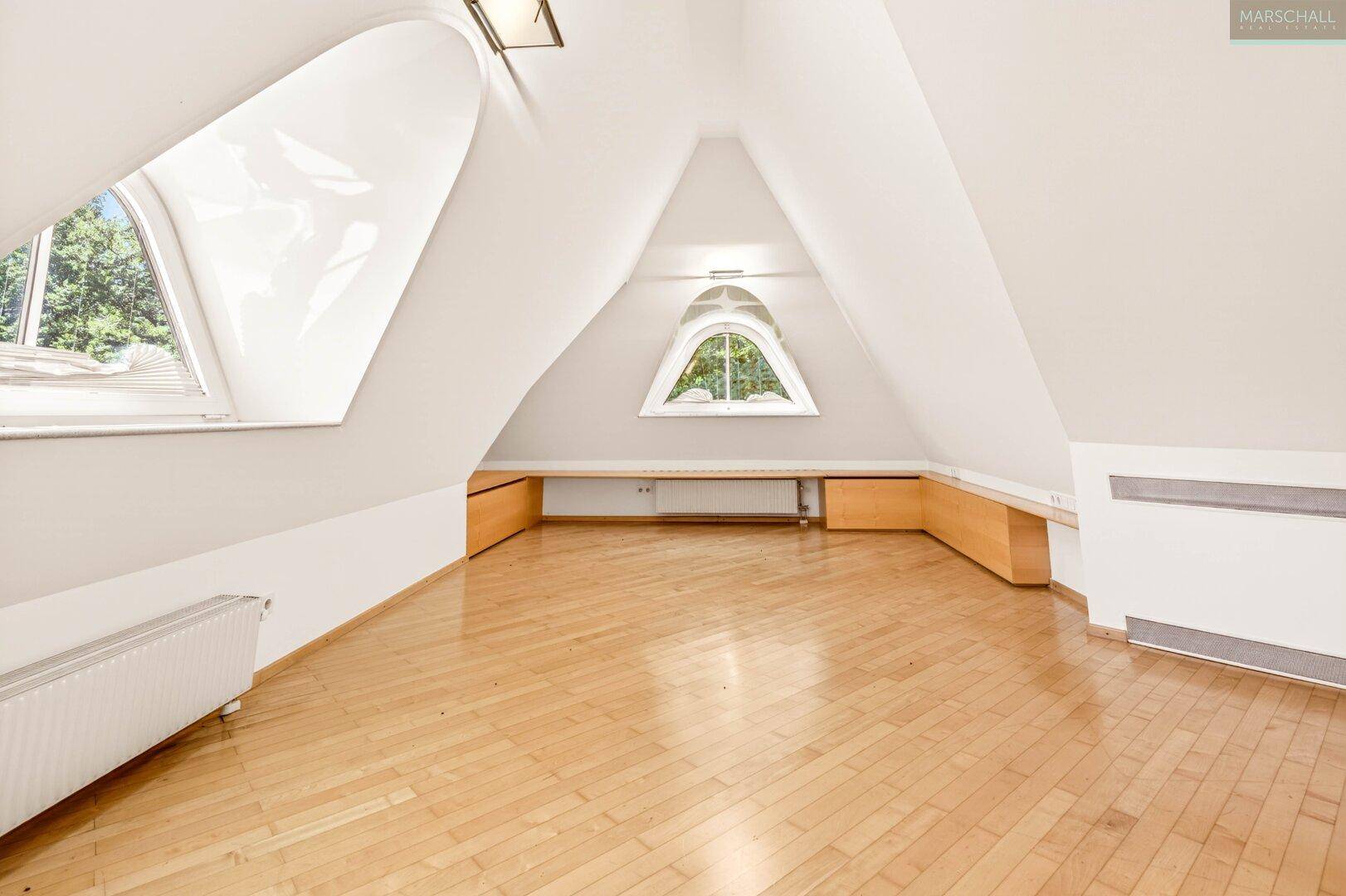 Helles Schlafzimmer im Dachgeschoss mit schrägen Wänden, Dachfenstern und Holzboden.