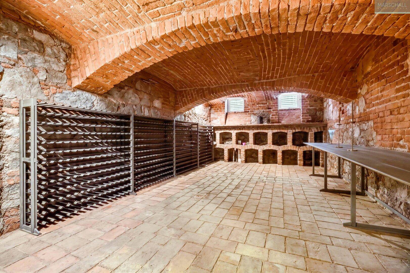 Historischer Weinkeller mit Ziegelgewölbe, Steinboden und umfangreichen Weinregalen.