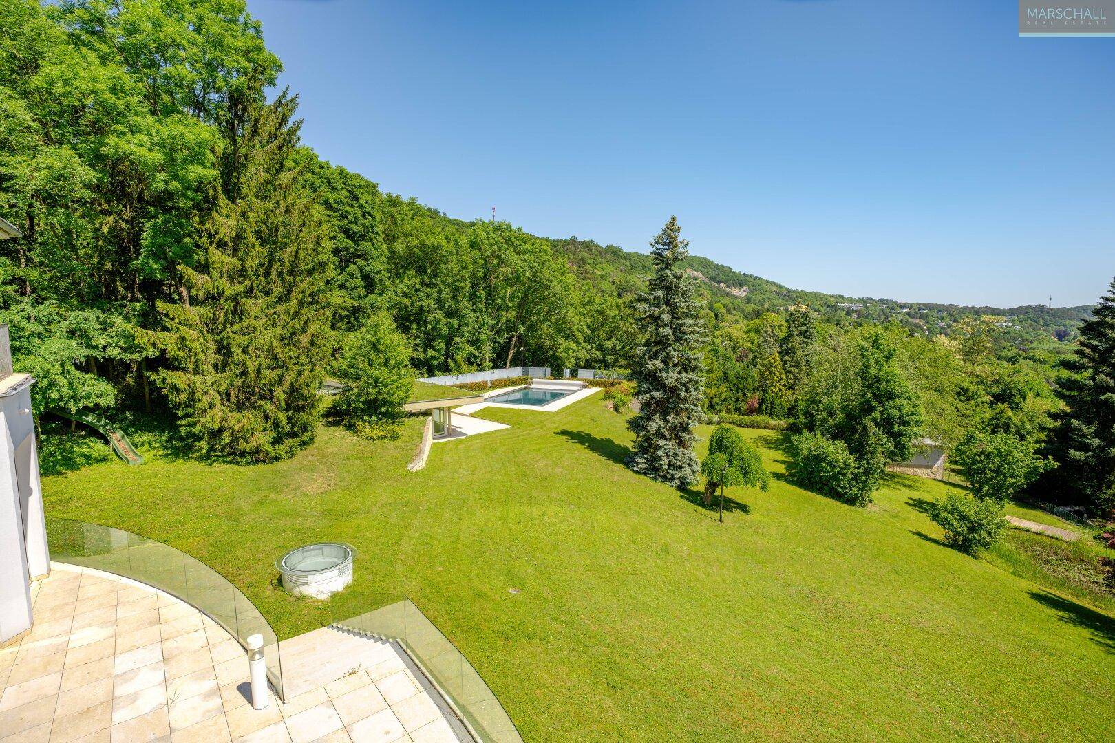 Panoramablick auf den weitläufigen Garten mit Pool und die umliegende bewaldete Landschaft.