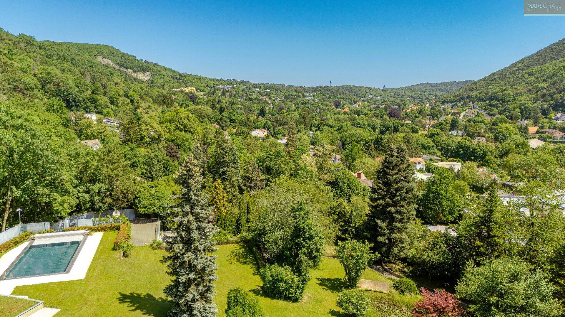 Panoramablick auf die grüne Landschaft mit bewaldeten Hügeln und Siedlungen im Tal.