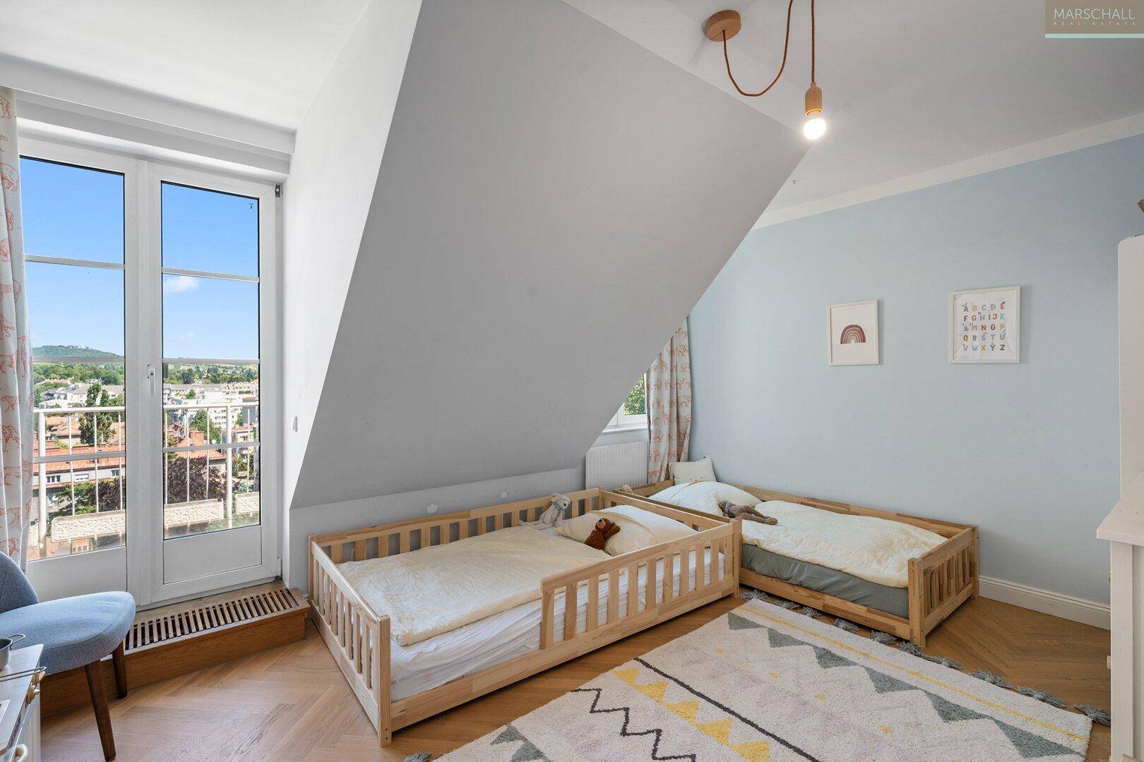 Kinderzimmer mit zwei Betten, Dachschräge, Fischgrätparkett und Zugang zum Balkon.