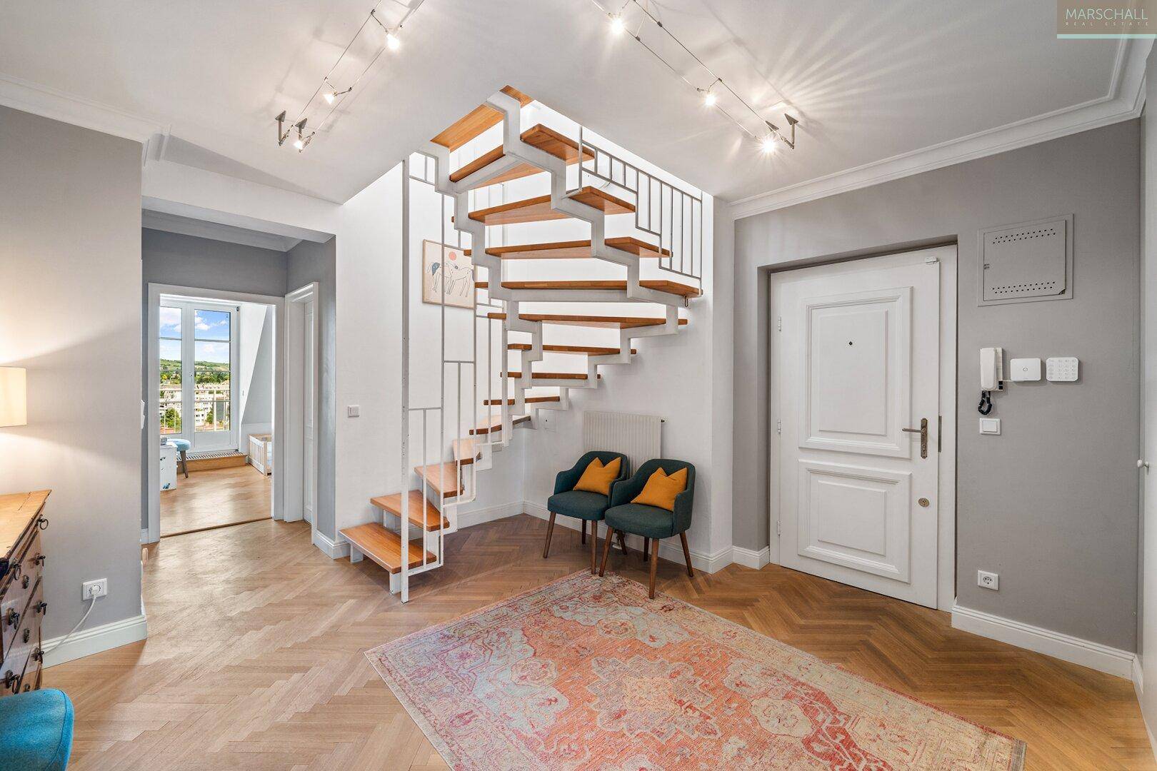Heller Eingangsbereich mit moderner Holztreppe, Fischgrätparkett und hohen Decken.