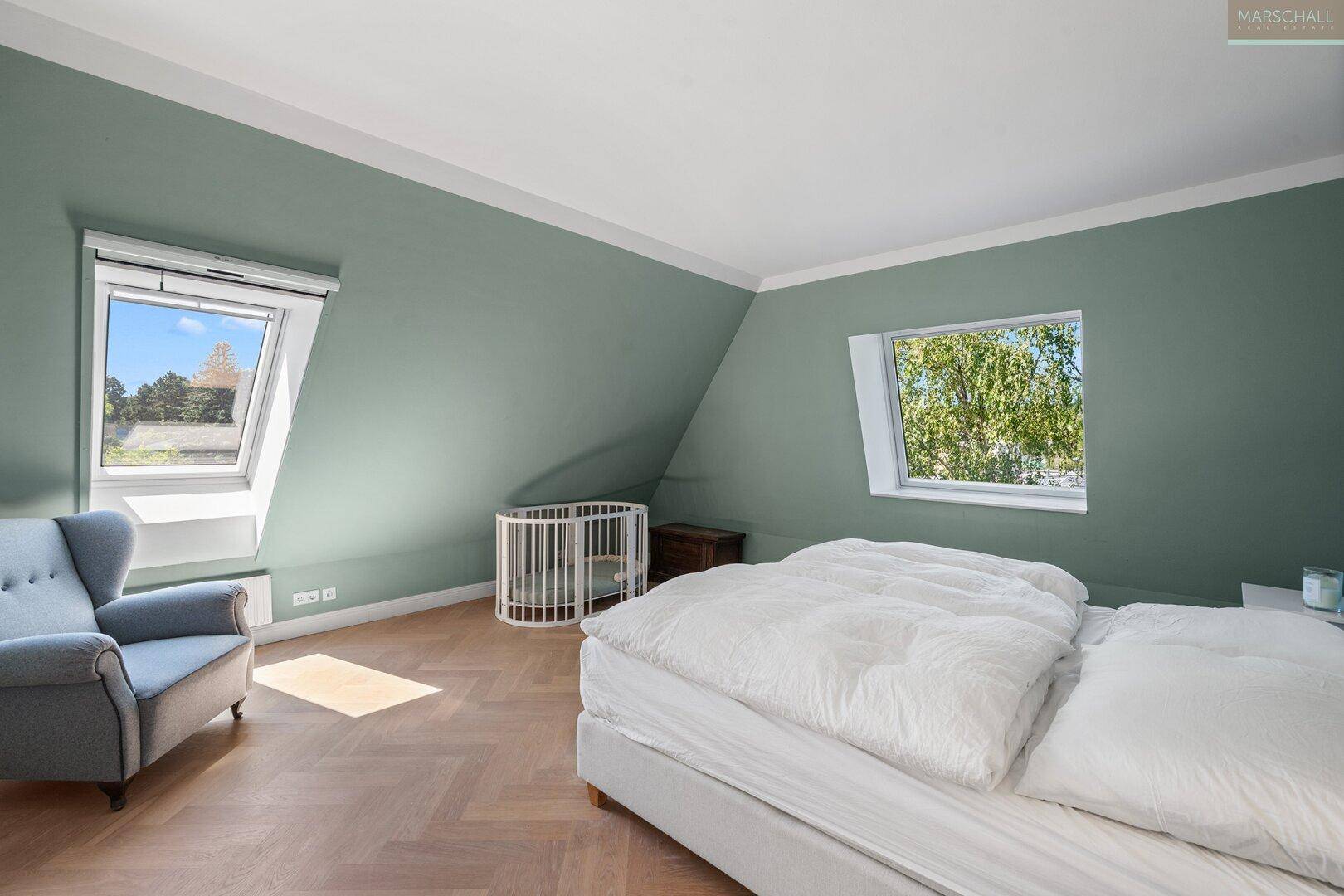 Großes Schlafzimmer mit Dachschrägen, Fischgrätparkett und zwei Dachfenstern.