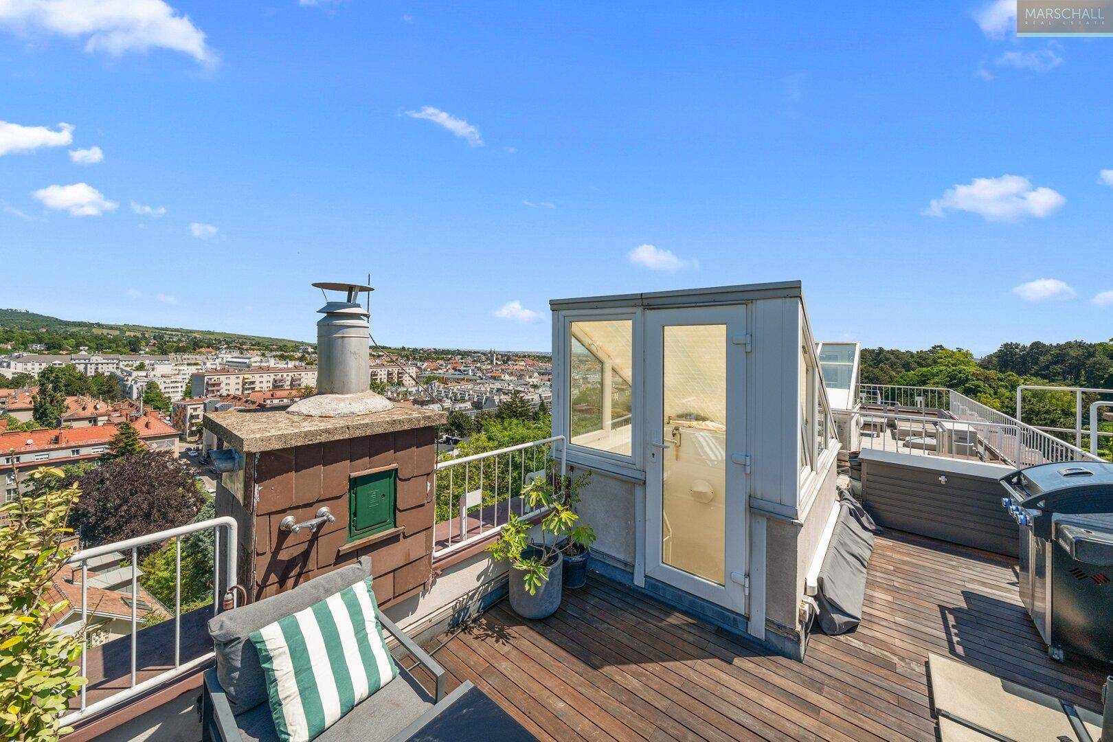 Weitläufige Dachterrasse mit Holzboden, Grillbereich und Panoramablick über die Stadt.