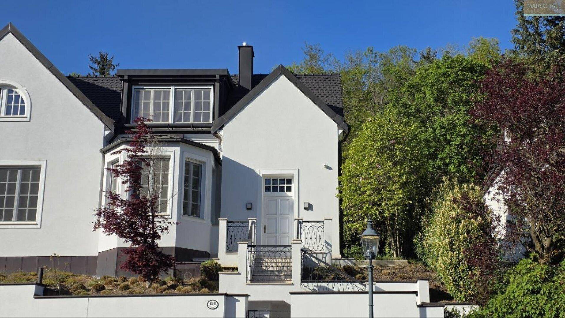 Vorderansicht der modernen Villa mit weißer Fassade und gepflegter Bepflanzung.
