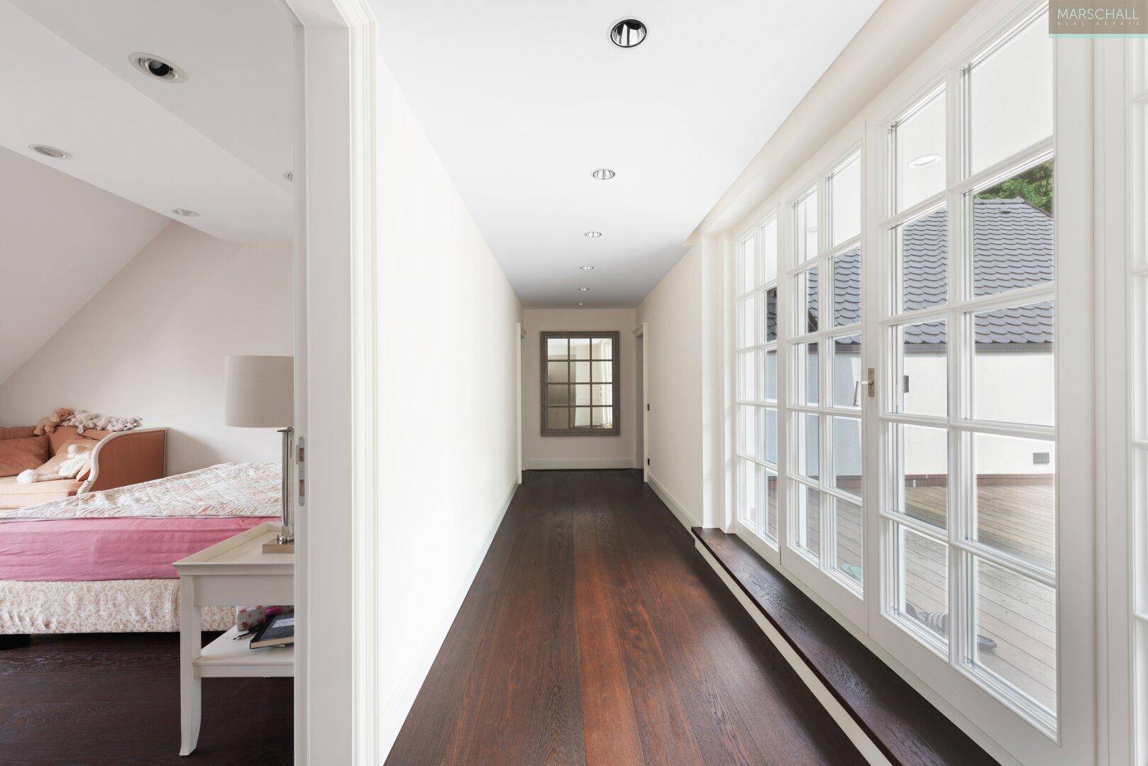 Heller Flur mit dunklem Holzboden und großen Fenstertüren, die nach außen führen.