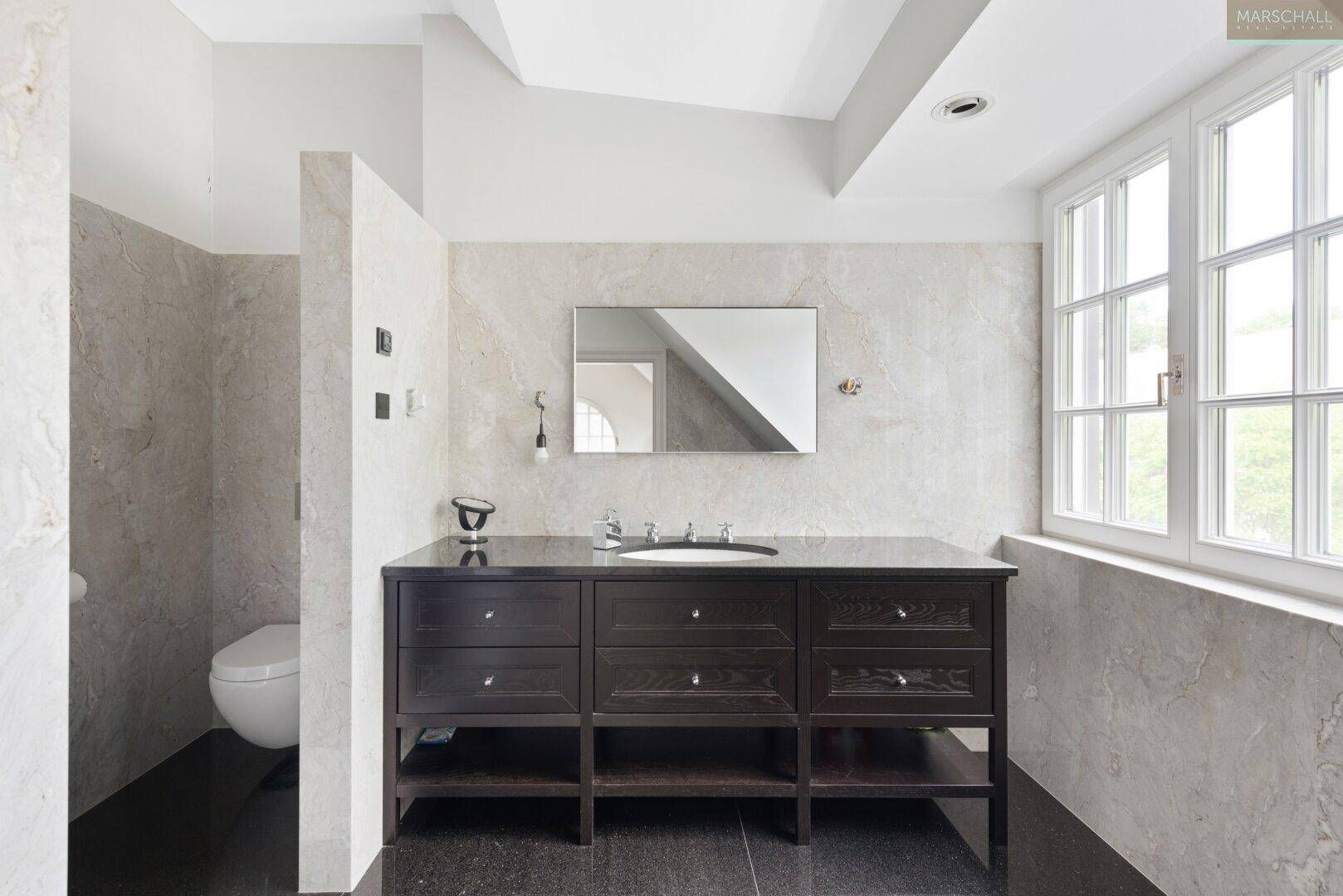 Modernes Badezimmer mit dunklem Waschtisch, Marmorwänden und separatem WC-Bereich.