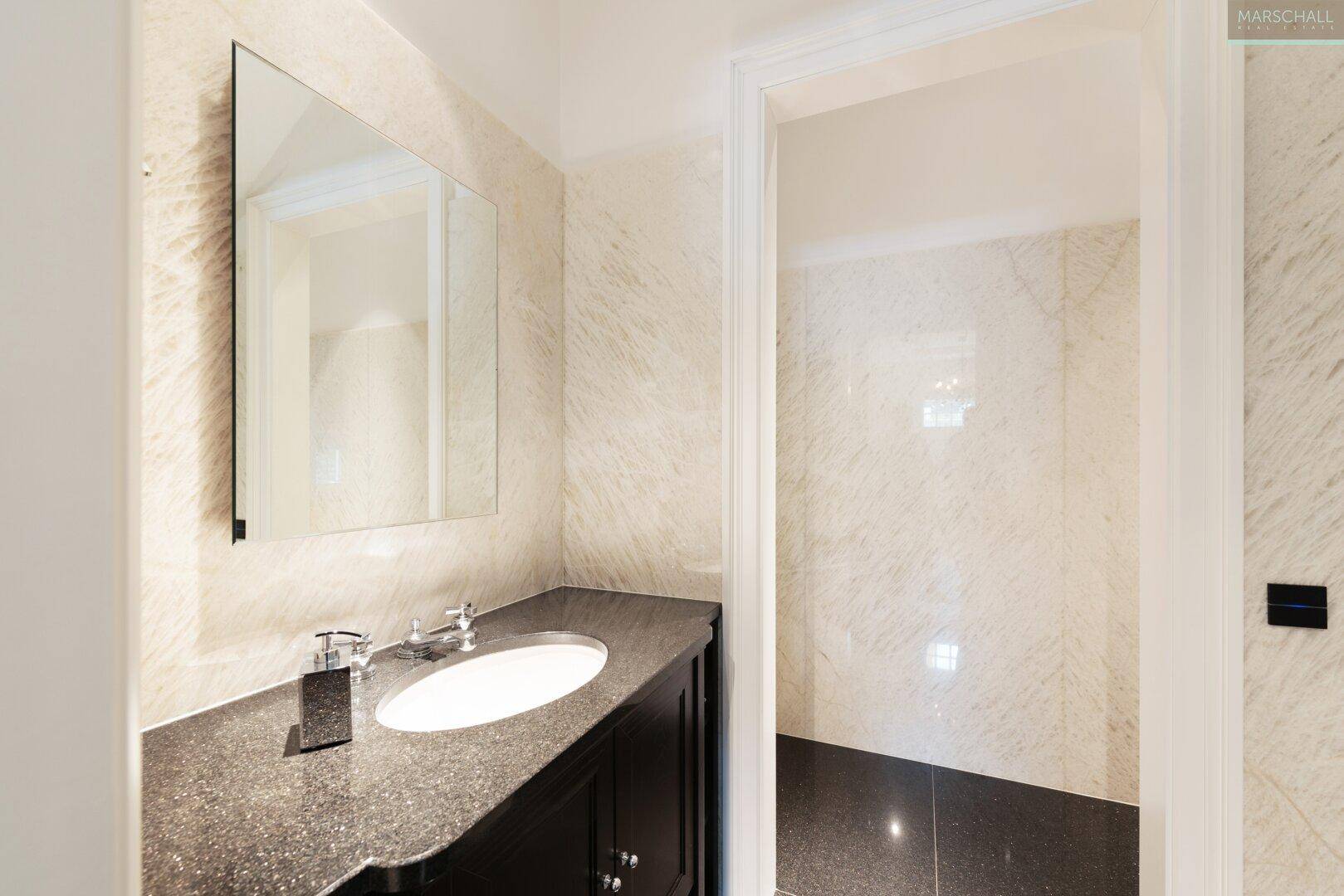 Kleines Gäste-WC mit dunklem Waschtisch, Marmorwänden und modernem Design.
