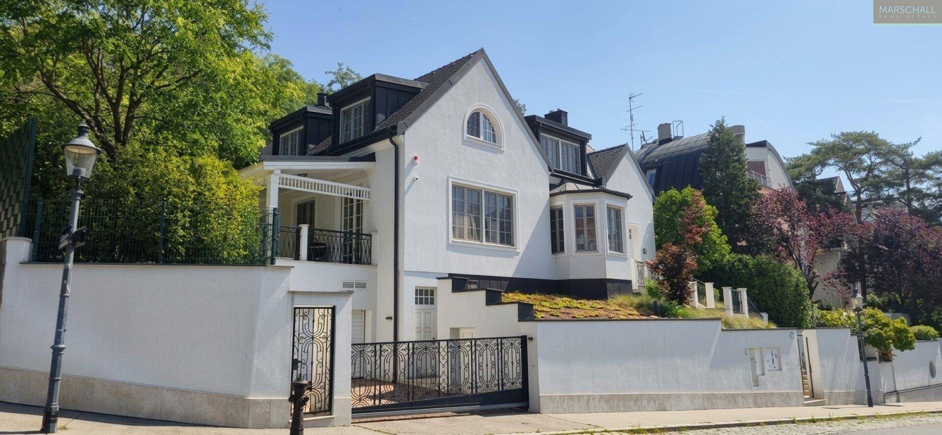 Weitläufige Ansicht des modernen Hauses mit Zufahrt und umliegender grüner Landschaft.