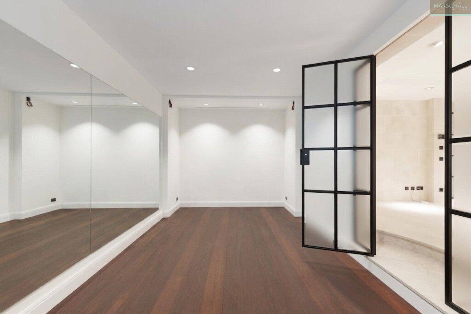 Vielseitiger Raum mit Spiegelwand, Holzboden und moderner Glastür, ideal als Fitnessbereich.