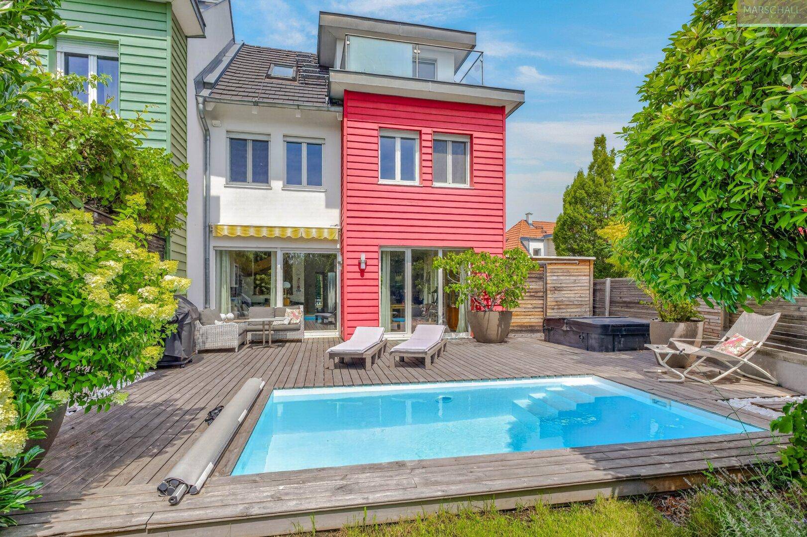 Rückansicht des modernen Reihenhauses mit Pool, Holzterrasse und roter Fassade.