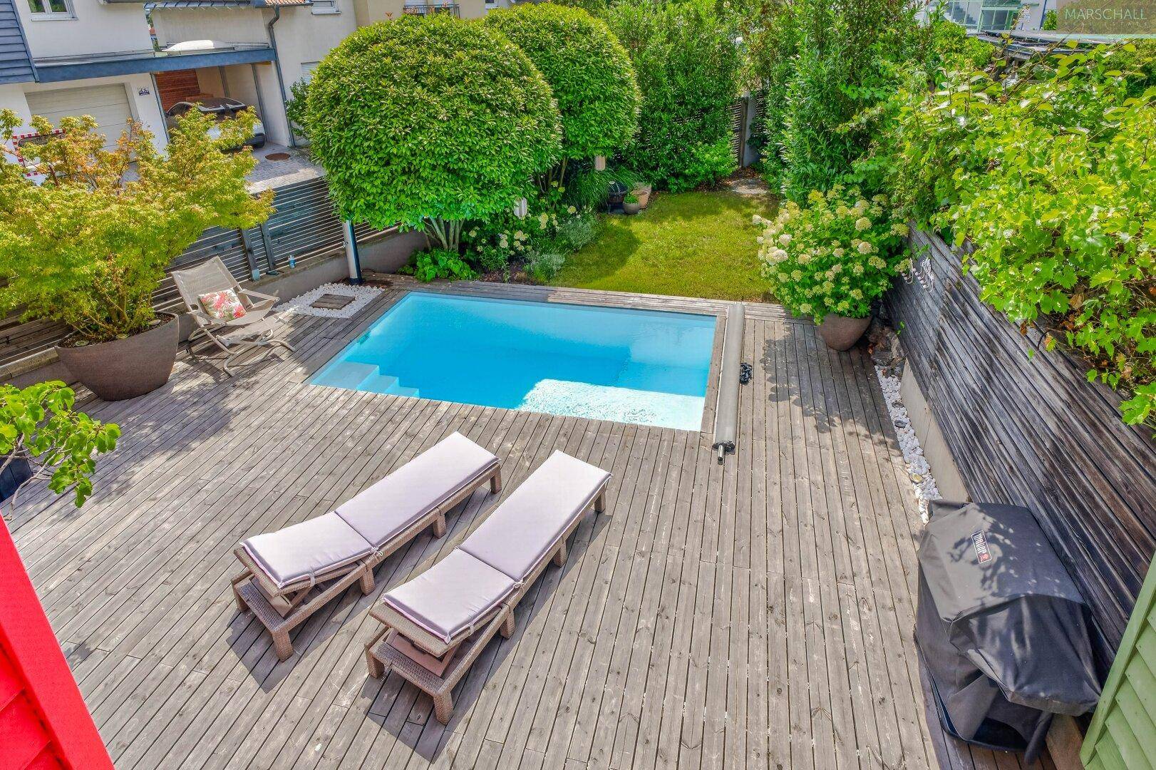 Vogelperspektive des Gartens mit Pool, Holzterrasse, Liegestühlen und Grillbereich.