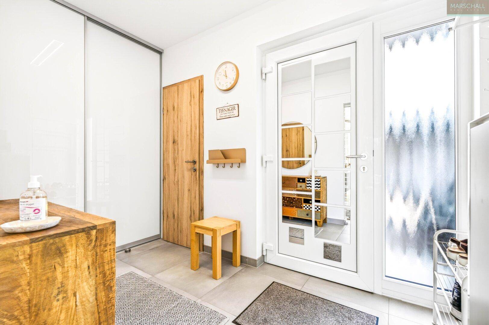 Eingangsbereich mit Fliesenboden, Holztür und Garderobe, hell und einladend gestaltet.