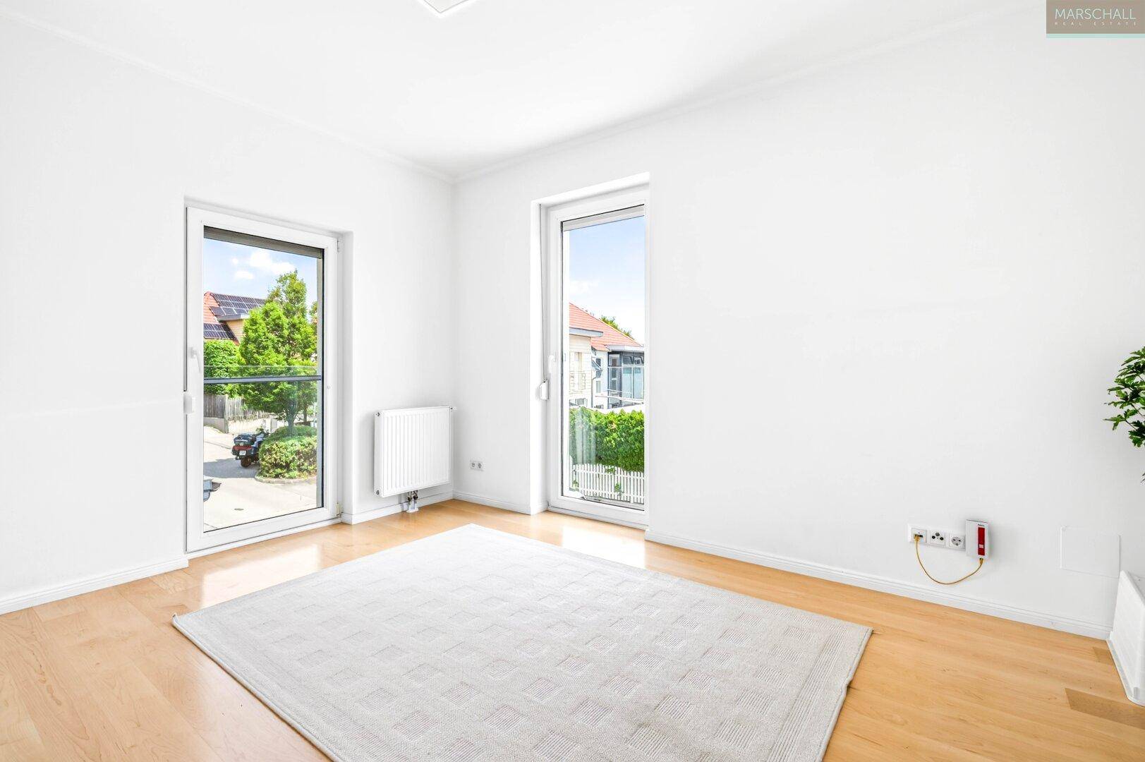 Heller Raum mit Holzboden und zwei großen Fenstertüren, ideal als Schlaf- oder Arbeitszimmer.