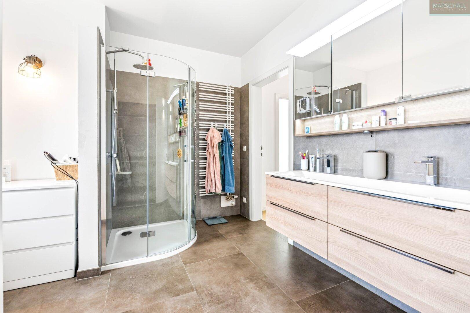 Modernes Badezimmer mit großer Dusche, Doppelwaschbecken und beheiztem Handtuchhalter.